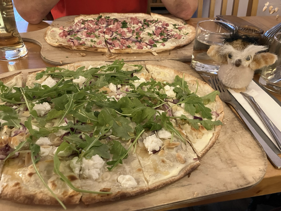 Zwei Bretter Flammkuchen, dahinter Hedi vor einem Glas Wasser